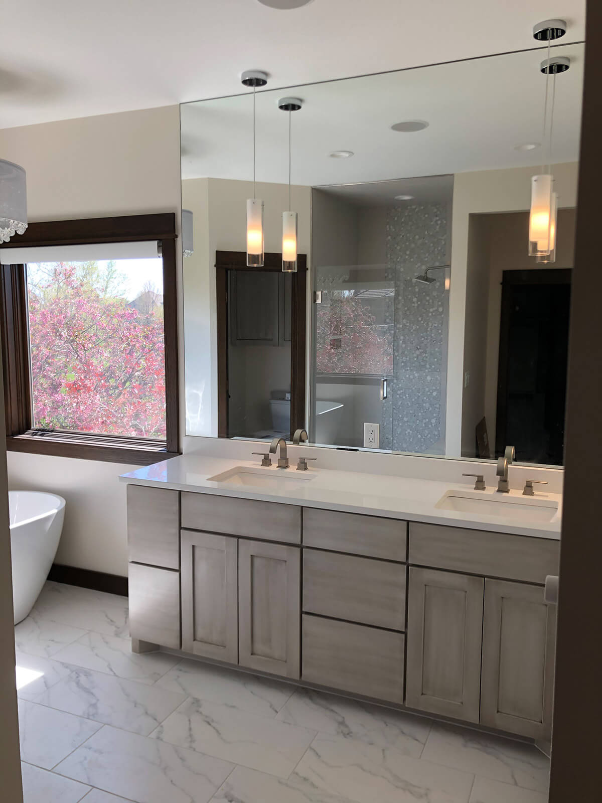 Light wood double vanity with white countertops and large wall mirror.