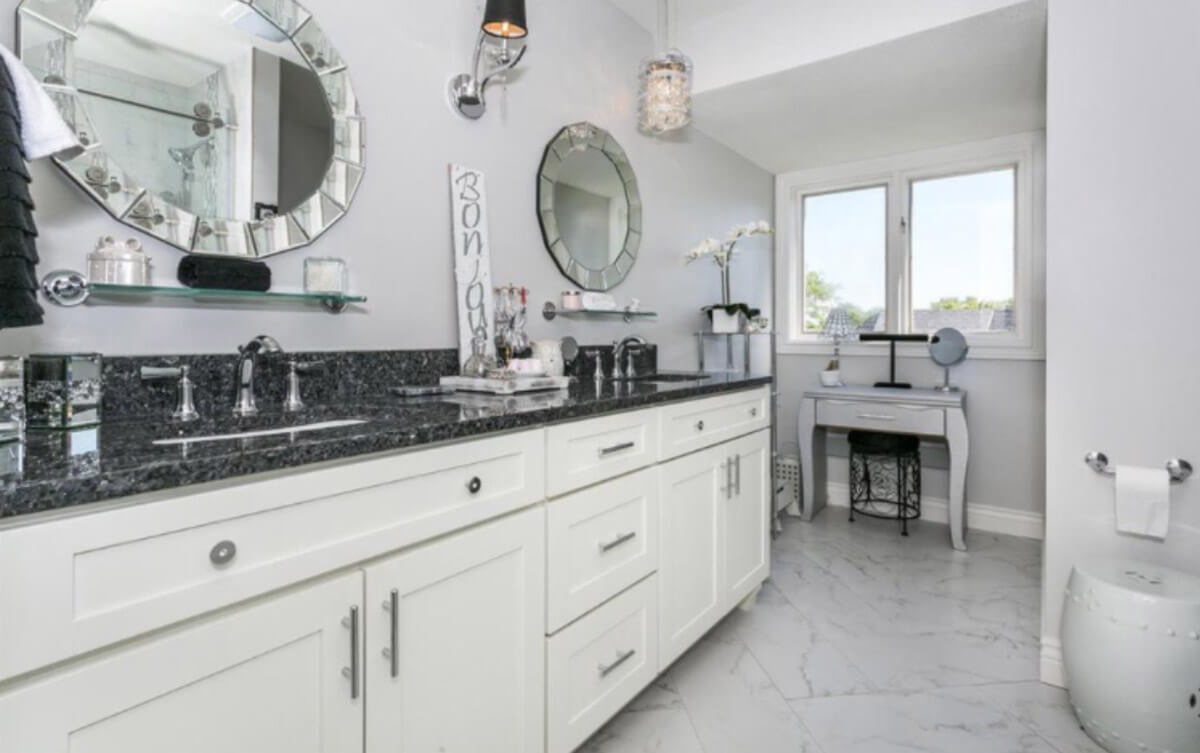 Bathroom double vanity with white cabinets,  black countertops and gray walls.
